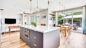 Eine moderne Küche mit Kochinsel, Esstisch aus Holz und Stühlen, verbunden mit einer großen Schiebeglastür, die zu einem Außenbereich führt.