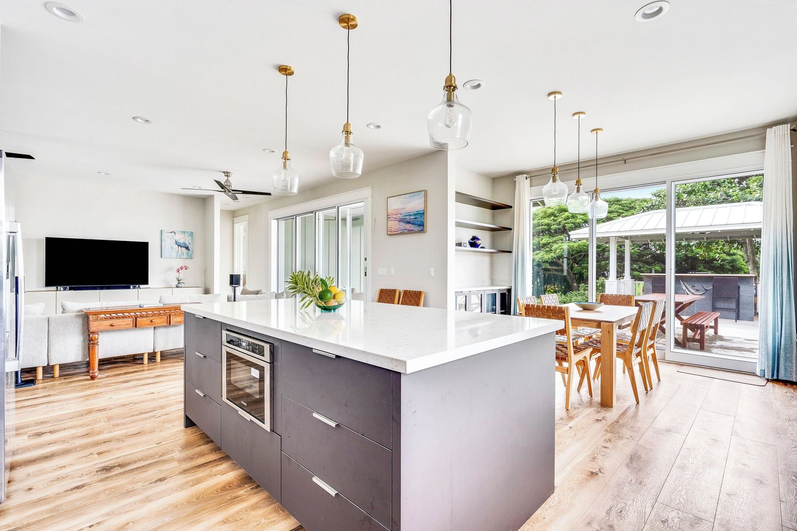 A modern kitchen with a central island, wooden flooring, and pendant lighting.