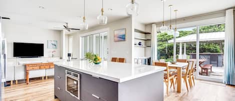 A modern kitchen with a central island, wooden flooring, and pendant lighting.
