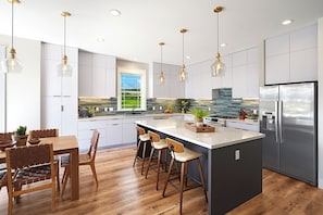 A modern kitchen with a central island, stainless steel appliances, pendant lighting, and a view of the outdoors.