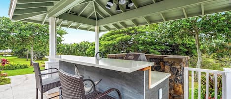 An outdoor bar area with a stone countertop, two wicker chairs, and a grill.