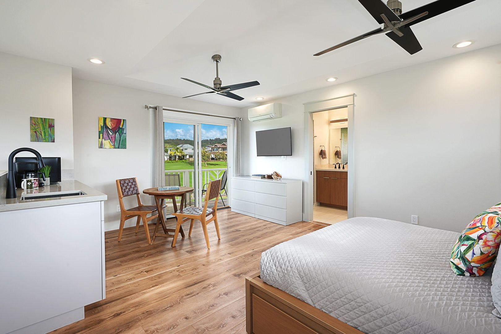 A bedroom with a bed, a desk with a chair, a television, and a balcony with a view.
