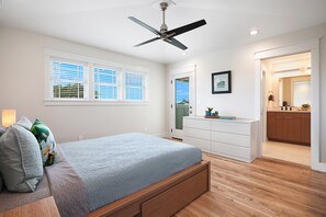 Een slaapkamer met een bed, een plafondventilator, een dressoir en een badkamer die door een open deur zichtbaar is.