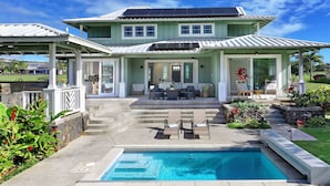 Ein zweistöckiges Haus mit Schwimmbad, Sitzgelegenheiten im Freien und einer überdachten Terrasse.