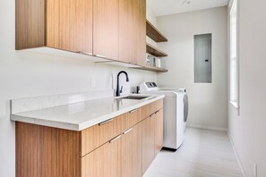 Una cocina moderna con armarios de madera, encimera blanca, un lavamanos y una lavadora.