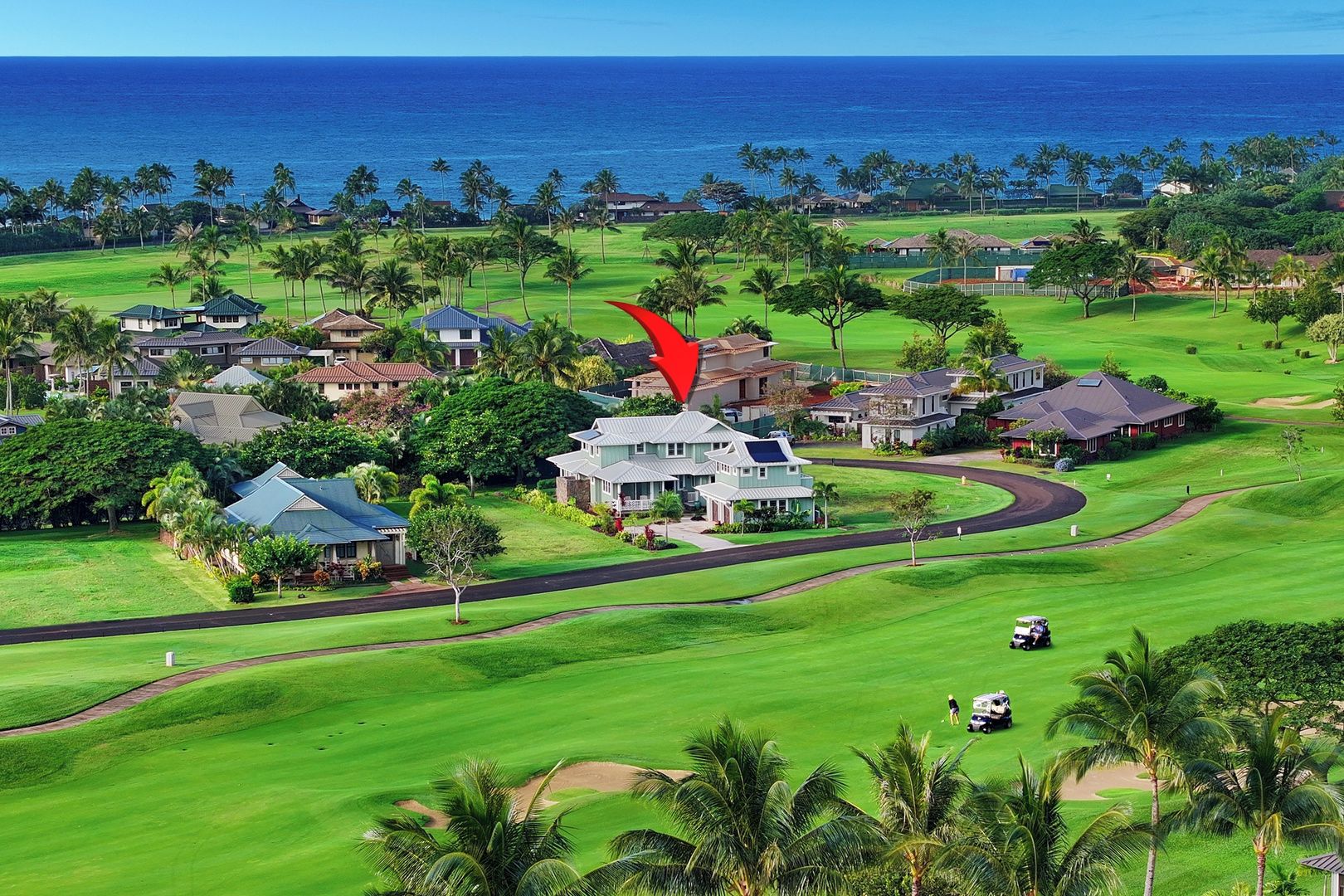 A golf course with a house in the center, surrounded by palm trees and a view of the ocean.