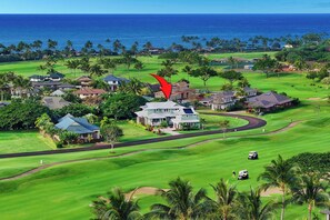 Een golfbaan met een huis in het midden, omringd door palmbomen en uitzicht op zee.