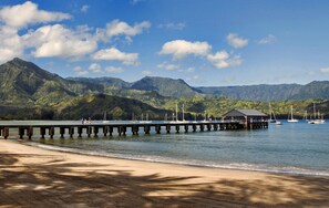 Una playa con un muelle que se adentra en aguas tranquilas, rodeada de montañas.