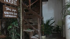 Un escalier en bois mène à une auberge de jeunesse. Une enseigne indique le nom de l’établissement : « JERIKITESURFHOSTEL », et affiche également les coordonnées.