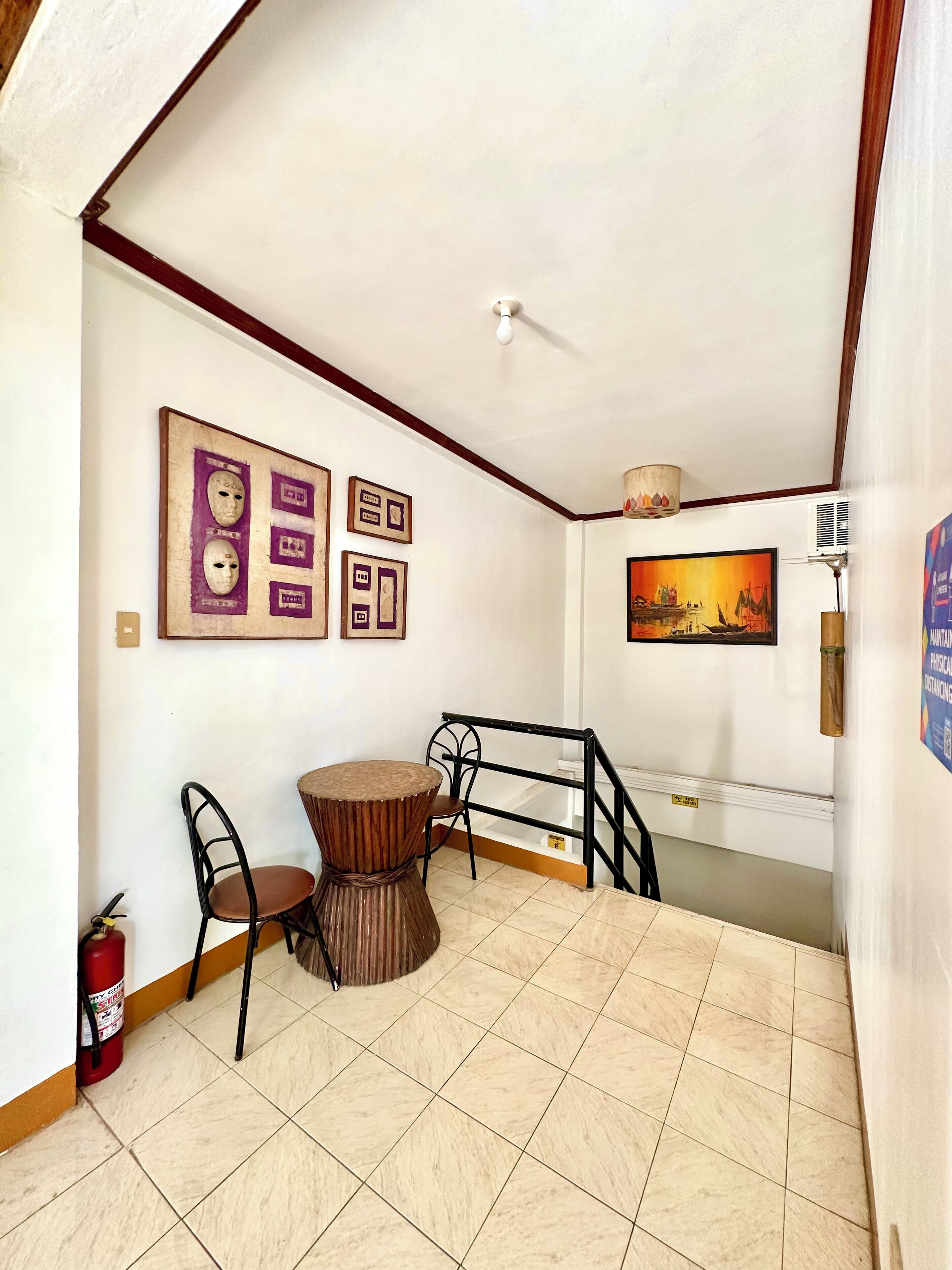 A small dining area with a round table and two chairs, a fire extinguisher, and a staircase with a railing.