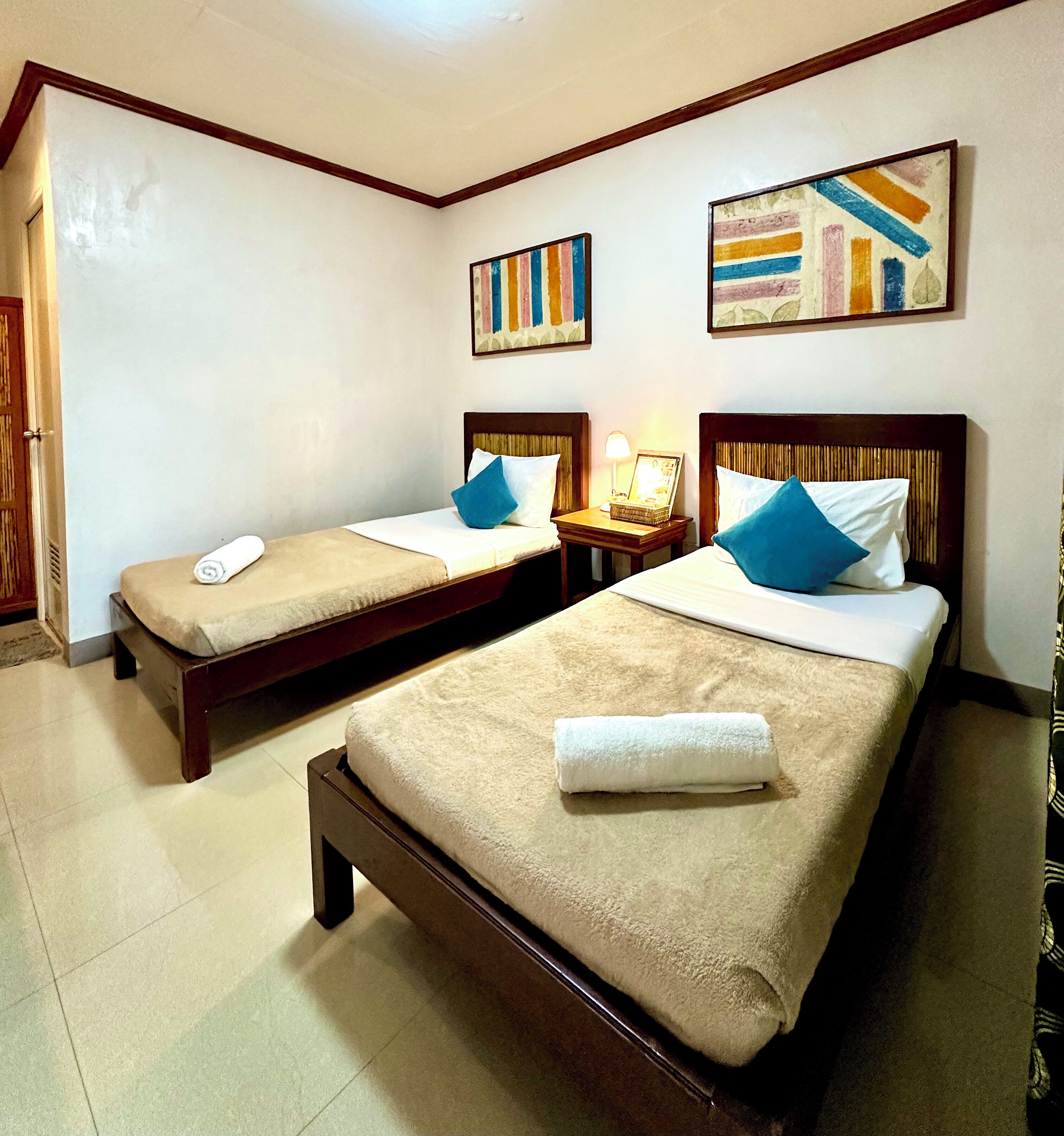 A hotel room with two single beds, each with a wooden headboard, a bedside table with a lamp, and a small picture frame.