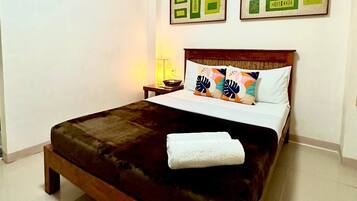 Una cama cuidadosamente tendida con un cabecero marrón oscuro, ropa de cama blanca y almohadas decorativas. Encima de la cama, hay cuadros enmarcados en la pared.