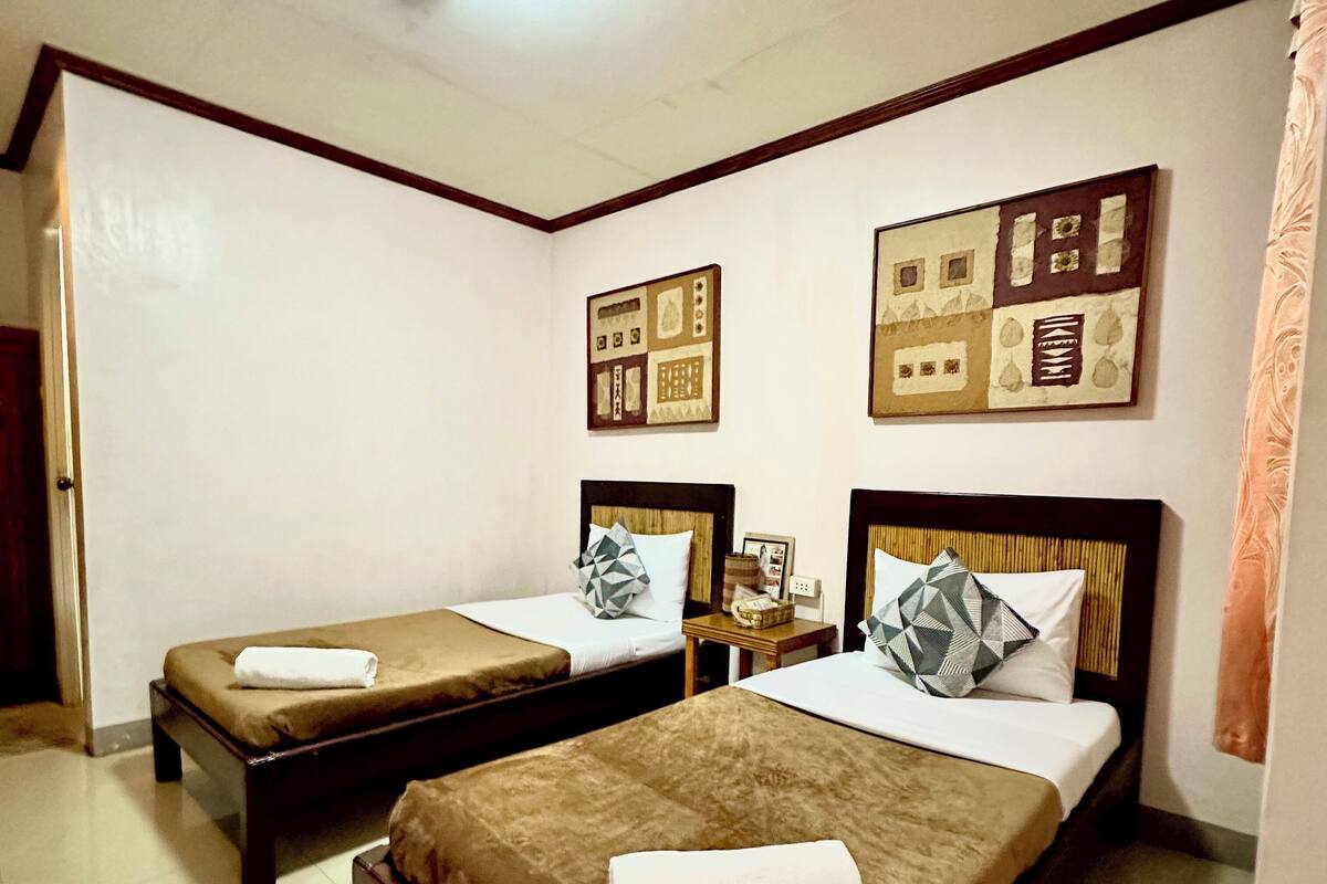 A hotel room with two beds, each with a brown bedspread and pillows, a small wooden nightstand, and framed pictures on the wall.