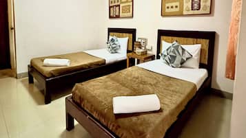 Una habitación de hotel con dos camas, cada una con colcha y almohadas marrones, una mesita de noche de madera y cuadros en la pared.