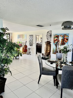 A spacious living room with a dining area, featuring a glass table, modern chairs, and a large potted plant.