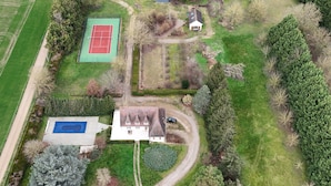 An aerial view of a residential area with a tennis court, a swimming pool, and a house with a driveway. - Villa Bien-être et Fête : Jacuzzi, Sauna, Court de Tennis, Piscine D'été, Étang (Cézy)