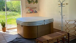 A modern bathroom with a freestanding bathtub, wooden benches, a drying rack, and shelves with plants. - Villa Bien-être et Fête : Jacuzzi, Sauna, Court de Tennis, Piscine D'été, Étang (Cézy)