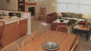 Un coin repas avec une table et des chaises, un espace cuisine équipé d’appareils électroménagers et une fenêtre avec des rideaux.
