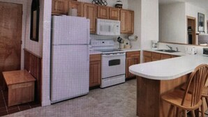 Une cuisine avec des meubles de rangement en bois, un réfrigérateur blanc, une cuisinière et un coin repas comprenant une table et des chaises.