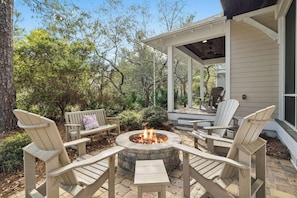A fire pit surrounded by Adirondack chairs, a bench, and a covered patio area.