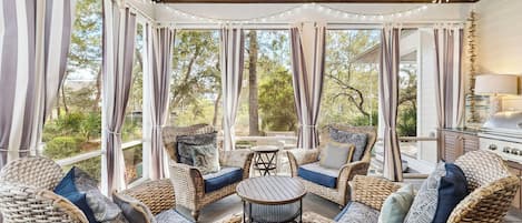 A covered outdoor seating area with wicker furniture, a round table, and a grill.