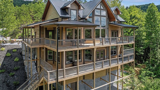A multi-level wooden house with balconies, large windows, and a view of a forested area.