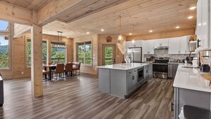 A modern kitchen with wooden beams, large windows, and a dining area with a view.