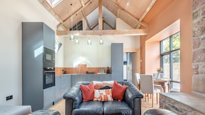 Een moderne woonkamer met een leren zwarte bank, een houten plafond en een keuken op de achtergrond.