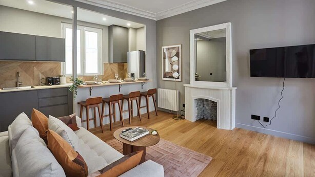 Un salon moderne avec un canapé, une table basse et un coin repas comprenant des chaises, et une cuisine en arrière-plan.