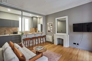A modern living room with a sofa, a coffee table, and a dining area with chairs and a kitchen in the background.