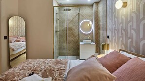 Une chambre moderne avec un grand lit, un miroir de chevet, une coiffeuse avec un miroir rond et une table de chevet avec une lampe.
