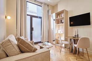 A modern living room with a sofa, a coffee table, a bookshelf, a TV, and a dining area.
