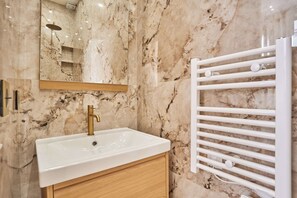 A bathroom with a marble wall, a white sink, a gold faucet, and a white towel rack.