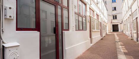 A narrow alleyway with white buildings, red-framed windows, and a brick pathway.