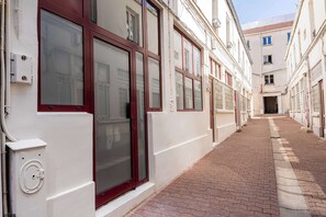 Uma viela estreita com edifícios brancos, janelas com molduras vermelhas e um caminho de tijolos.