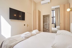 A hotel room with a bed, a flat-screen TV mounted on the wall, a wooden door, and a window with curtains.