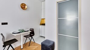 A modern dining area with a white table, two black chairs, and a small round table with a plant. - Cosi apartment Bastille-Le Marais (Paris)