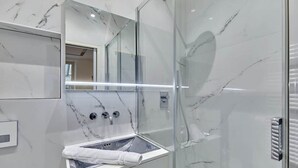 A modern bathroom with a glass-enclosed shower, a marble-tiled wall, and a built-in sink with a towel rack. - Cosi apartment Bastille-Le Marais (Paris)