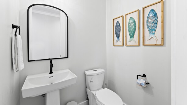 Un baño moderno con un lavamanos blanco, un inodoro y tres cuadros con peces enmarcados en la pared.