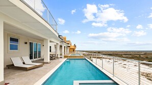 Un área junto a la piscina con sillones de descanso, una pequeña mesa y vistas a la playa.