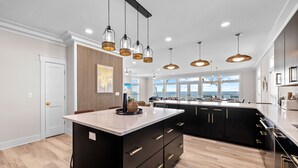 A modern kitchen with a large island, pendant lighting, and a view to the outside. - Water's Edge: Brand New Luxury Beachfront Home with Elevated Pool. Pet Friendly1 (Mexico Beach)