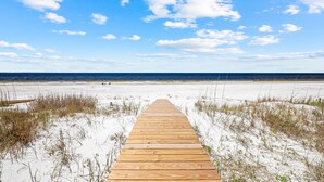 A wooden boardwalk leading to a beach with white sand and sparse vegetation. - Water's Edge: Brand New Luxury Beachfront Home with Elevated Pool. Pet Friendly1 (Mexico Beach)