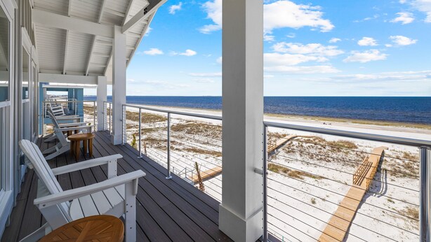 A covered deck with white chairs and a wooden table, overlooking a sandy beach and the ocean. - Water's Edge: Brand New Luxury Beachfront Home with Elevated Pool. Pet Friendly1 (Mexico Beach)