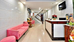 A hotel lobby with a reception desk, a staircase, and a pink sofa area.