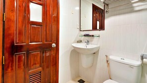 A bathroom with a wooden door, a white sink, a toilet, and a mirror above the sink. - S79 Residences Charisse (Ho Chi Minh City)