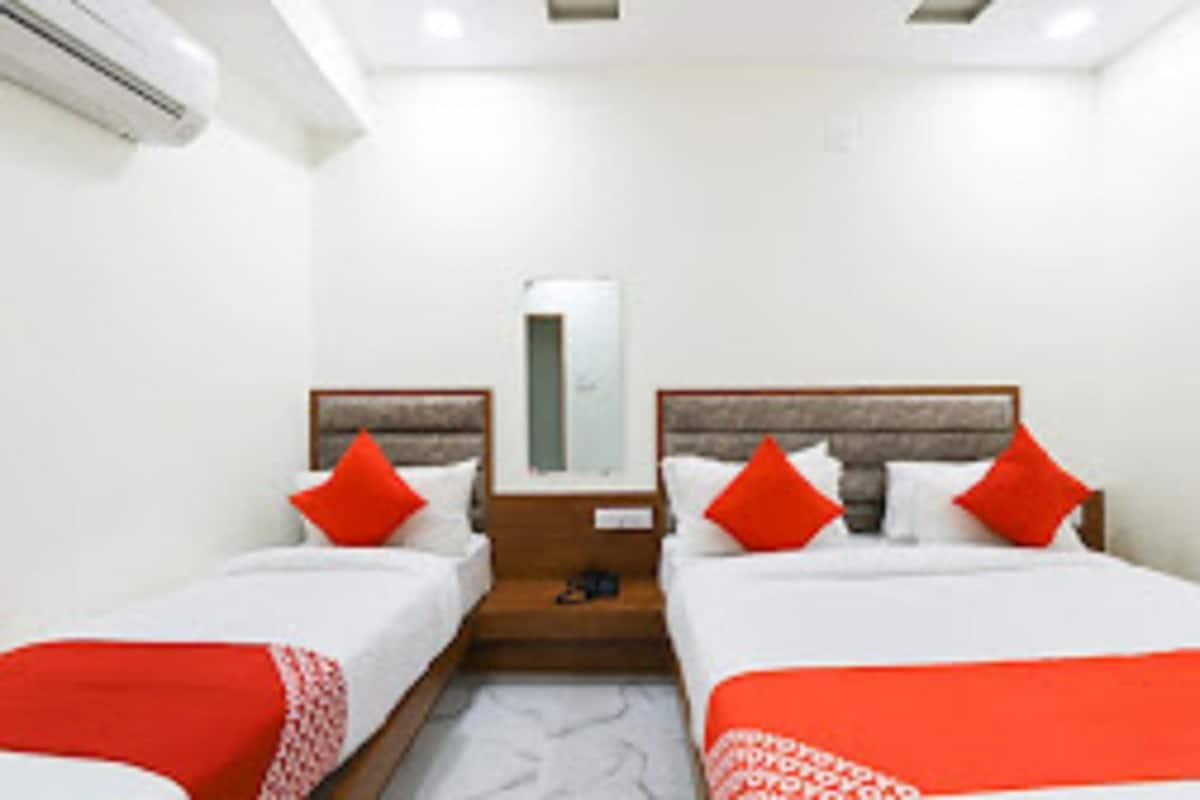 A hotel room with two beds, a nightstand, a mirror, and an air conditioning unit.