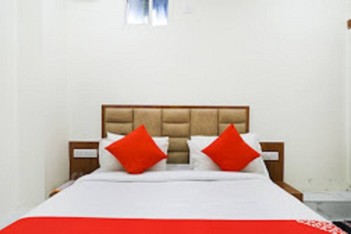 A bed with a wooden headboard, white bedding, and two red pillows.