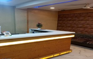 A reception desk with a wooden finish and a white top, a potted plant, and a sign with a QR code. - Hotel Sunrise Inn (Ahmedabad)