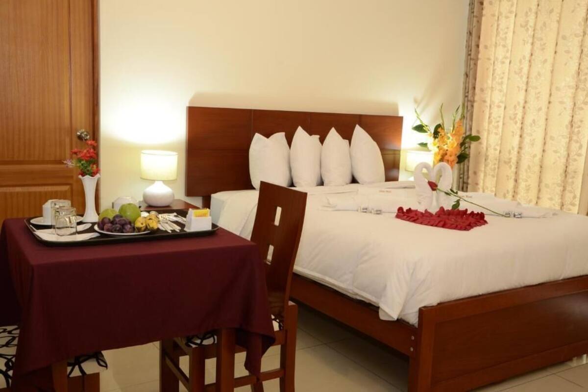 Ein Hotelzimmer mit einem ordentlich bezogenen Bett, einem kleinen Tisch mit einer Obstschale und einer Vase mit Blumen.