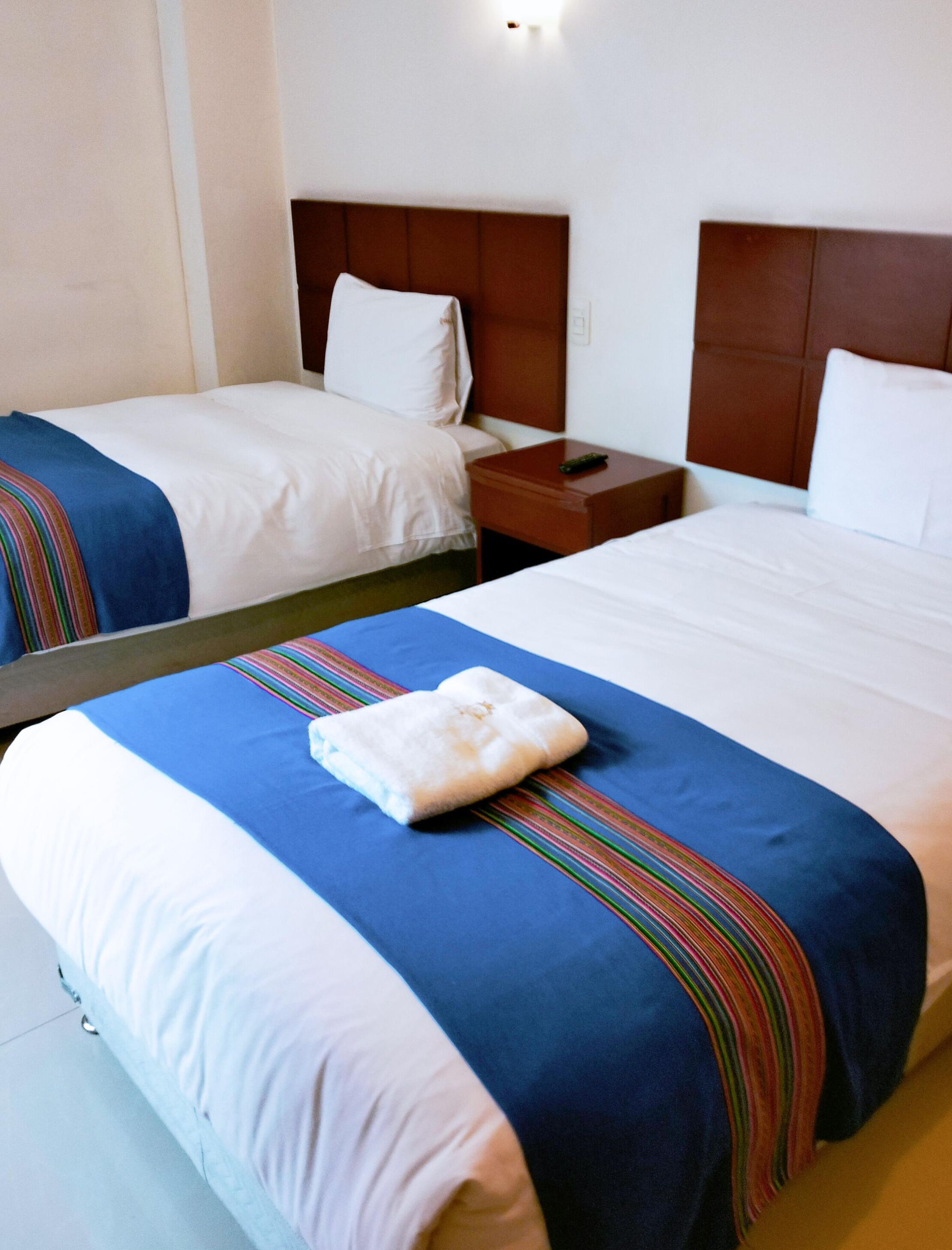 Ein Hotelzimmer mit zwei Betten, jeweils mit einer blauen und weißen Tagesdecke, einem hölzernen Kopfteil und einem Nachttisch mit einer Fernbedienung.